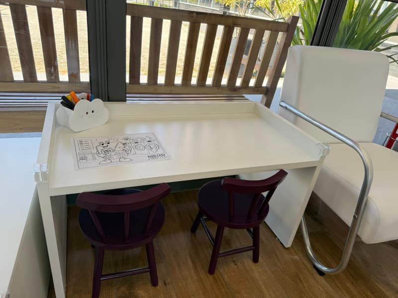 Mesinha branca com duas cadeirinhas roxas, giz de cera num porta-lápis em forma de nuvem e um desenho para colorir sobre a mesa